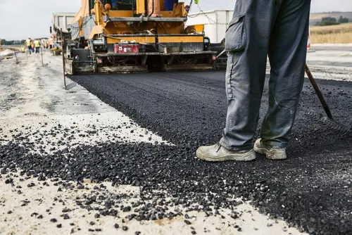 Worker applying bitumen during road construction